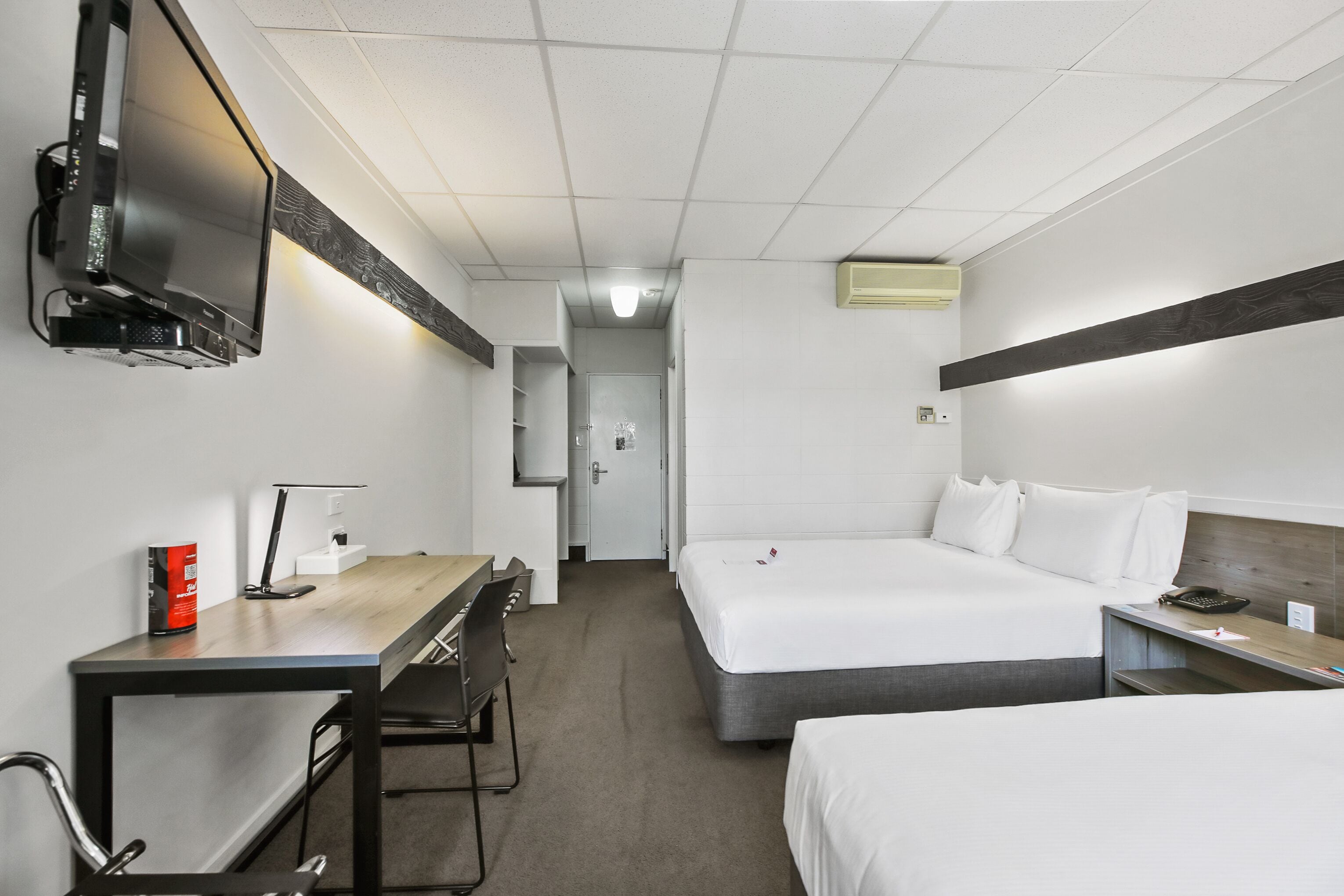 Habitación de hotel con dos camas, un escritorio, una silla, un televisor y una puerta que da a un baño.