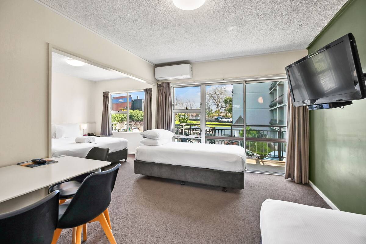 A hotel room with a bed, a desk, chairs, a TV, and a large window with a view of the outside.