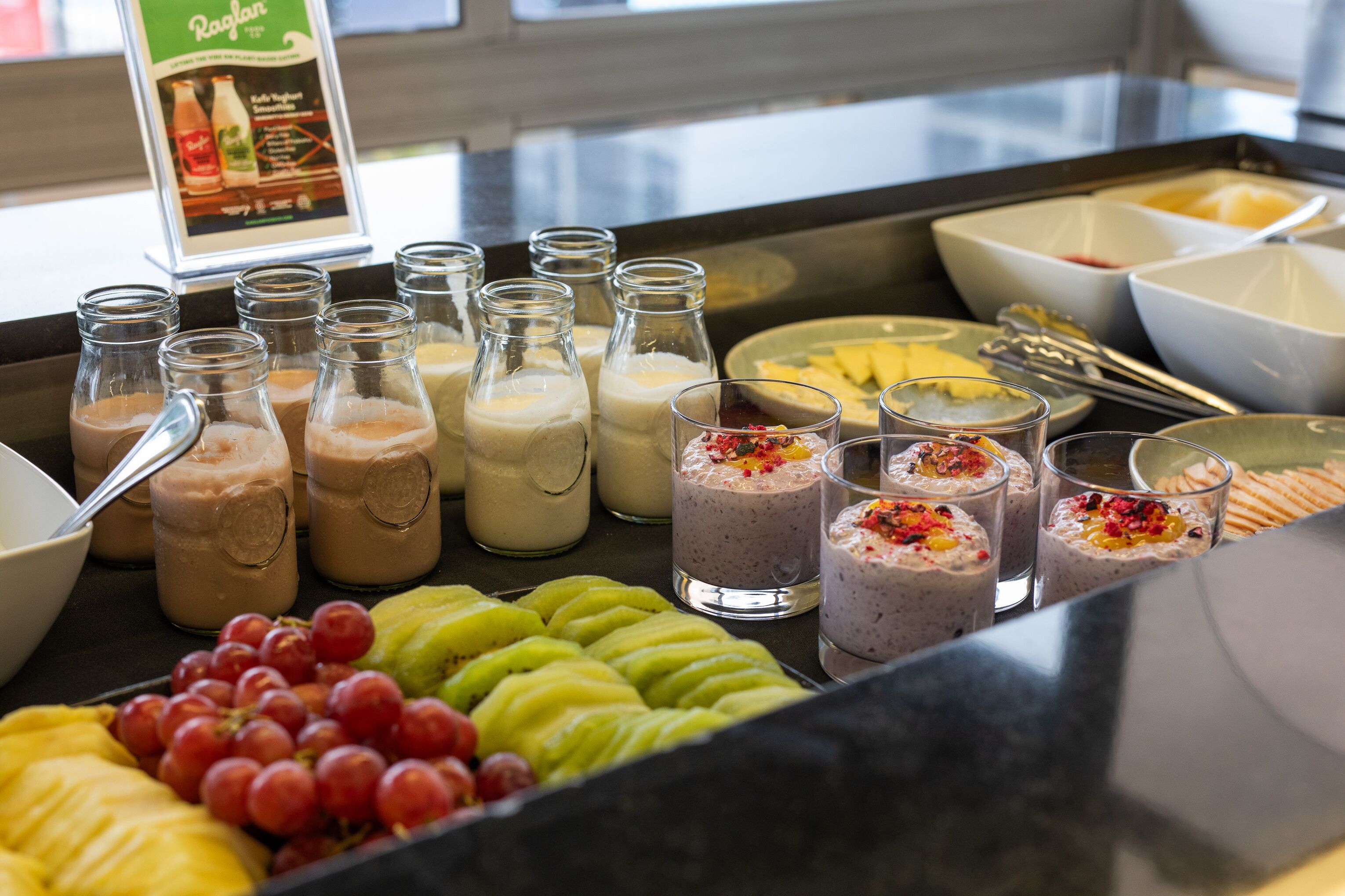 Un bufé con diversas opciones de comida y bebida, incluyendo frutas, batidos y tazones de yogur.