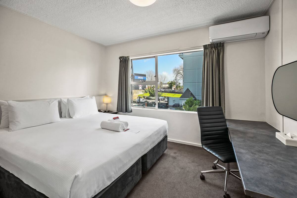 A hotel room with a bed, a desk, and a view of the outside.
