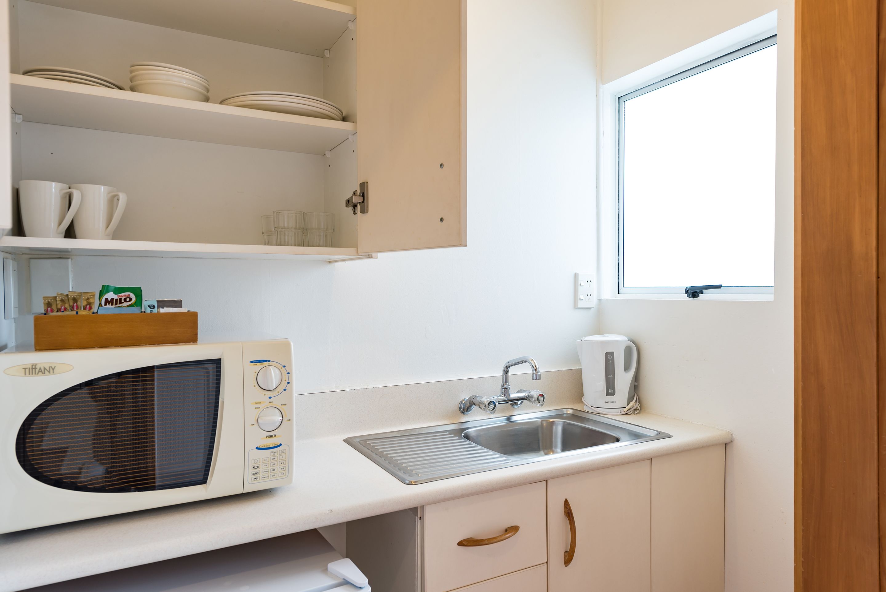 Una cocina compacta con microondas, lavamanos y armarios.