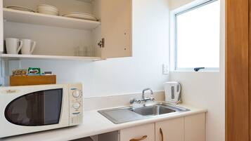 Una cocina compacta con microondas, lavamanos y armarios.