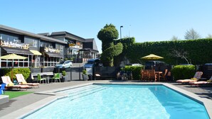 A swimming pool with lounge chairs and umbrellas, a restaurant with outdoor seating, and a well-maintained hedge. - Heartland Ambassador Hotel Hamilton (Hamilton)