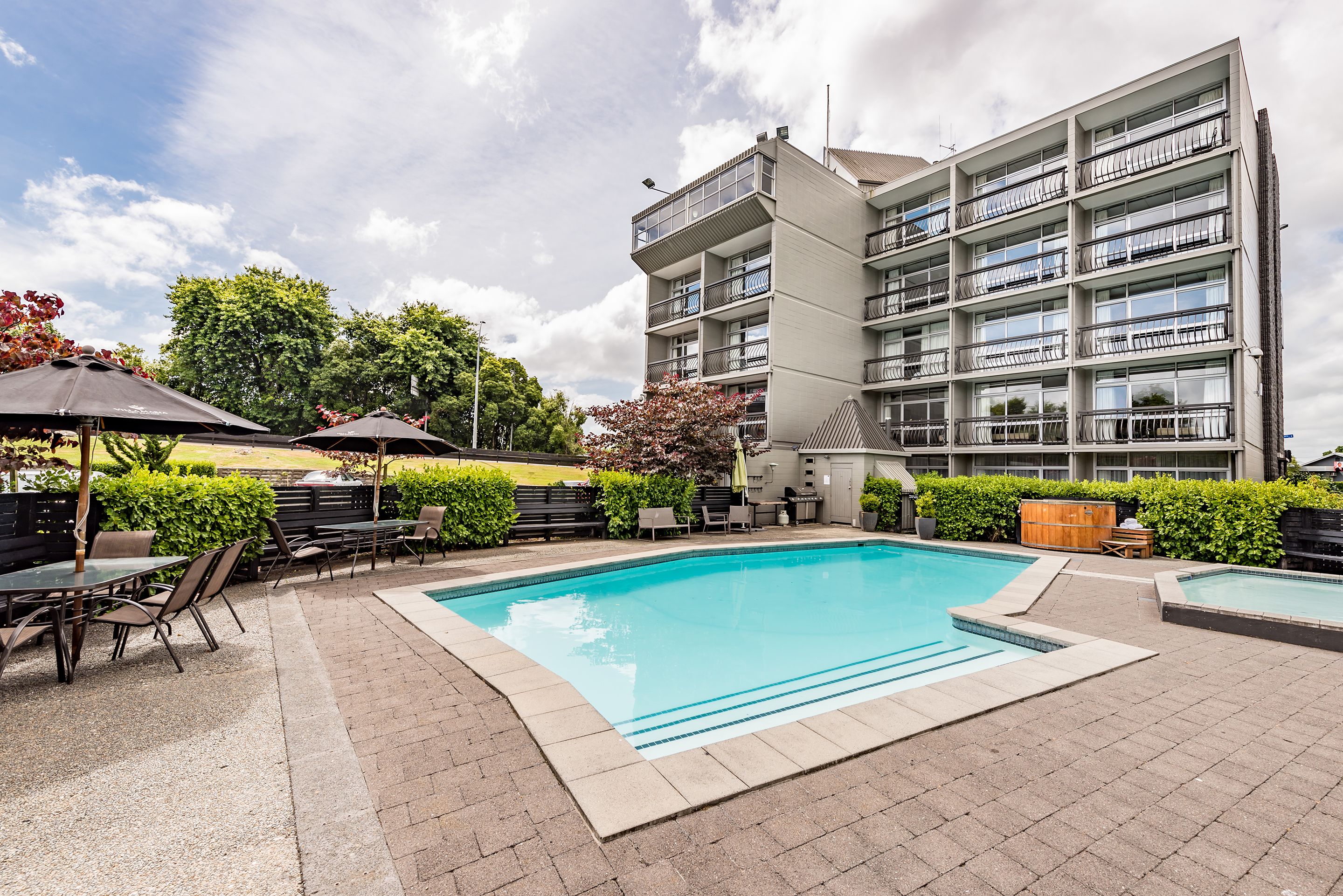 A modern building with a swimming pool, outdoor seating, and a well-maintained garden.