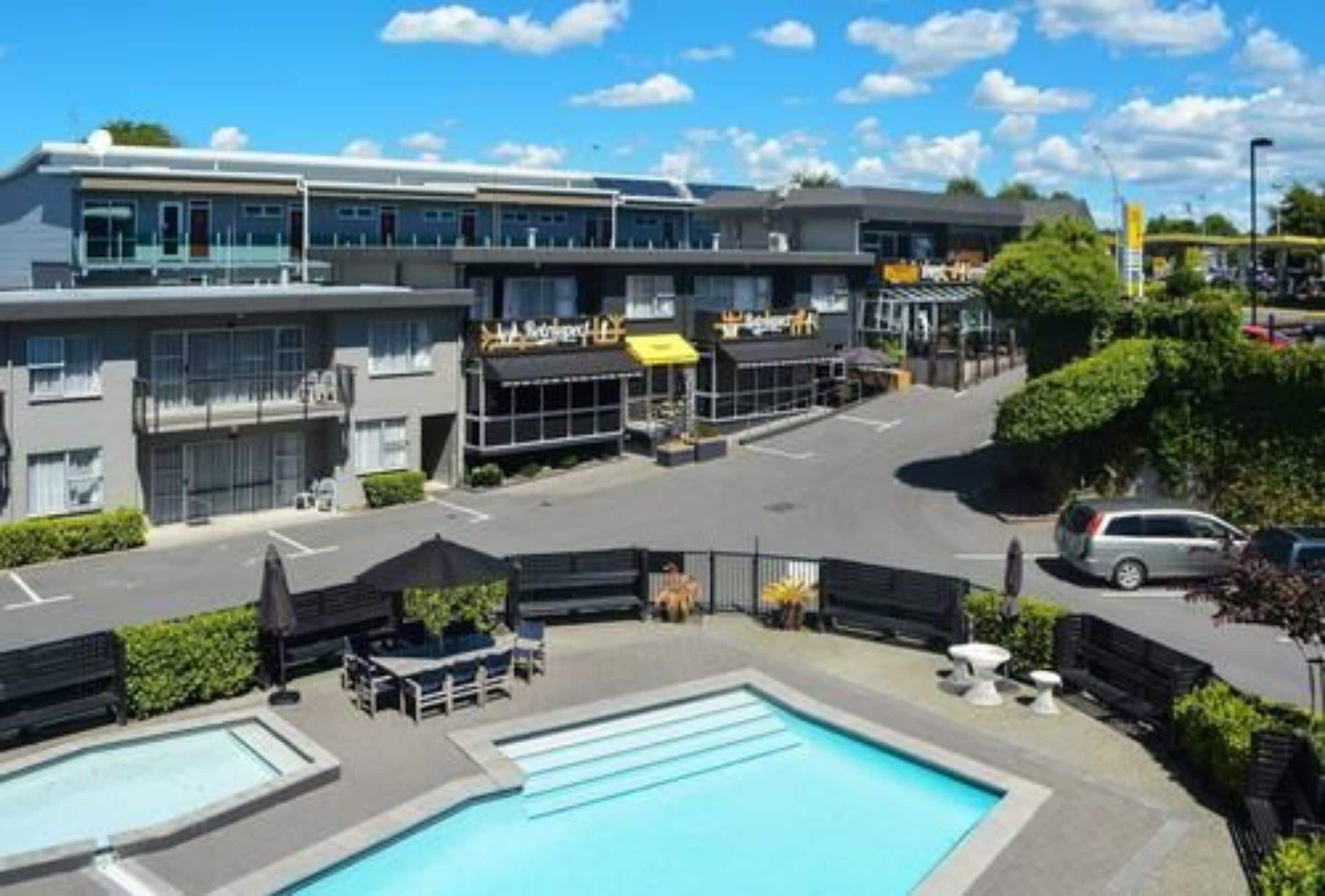 A hotel with a swimming pool, outdoor seating, and a parking lot.