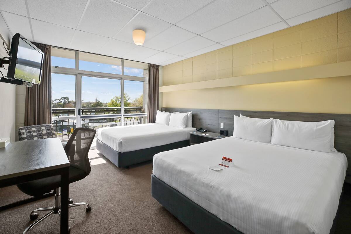 A hotel room with two beds, a desk, and a TV.