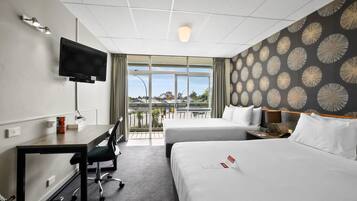 A hotel room with a desk, two beds, a TV, and a view of the outdoors.
