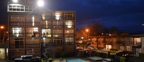 A multi-story hotel with a swimming pool, parking area, and a well-lit facade.