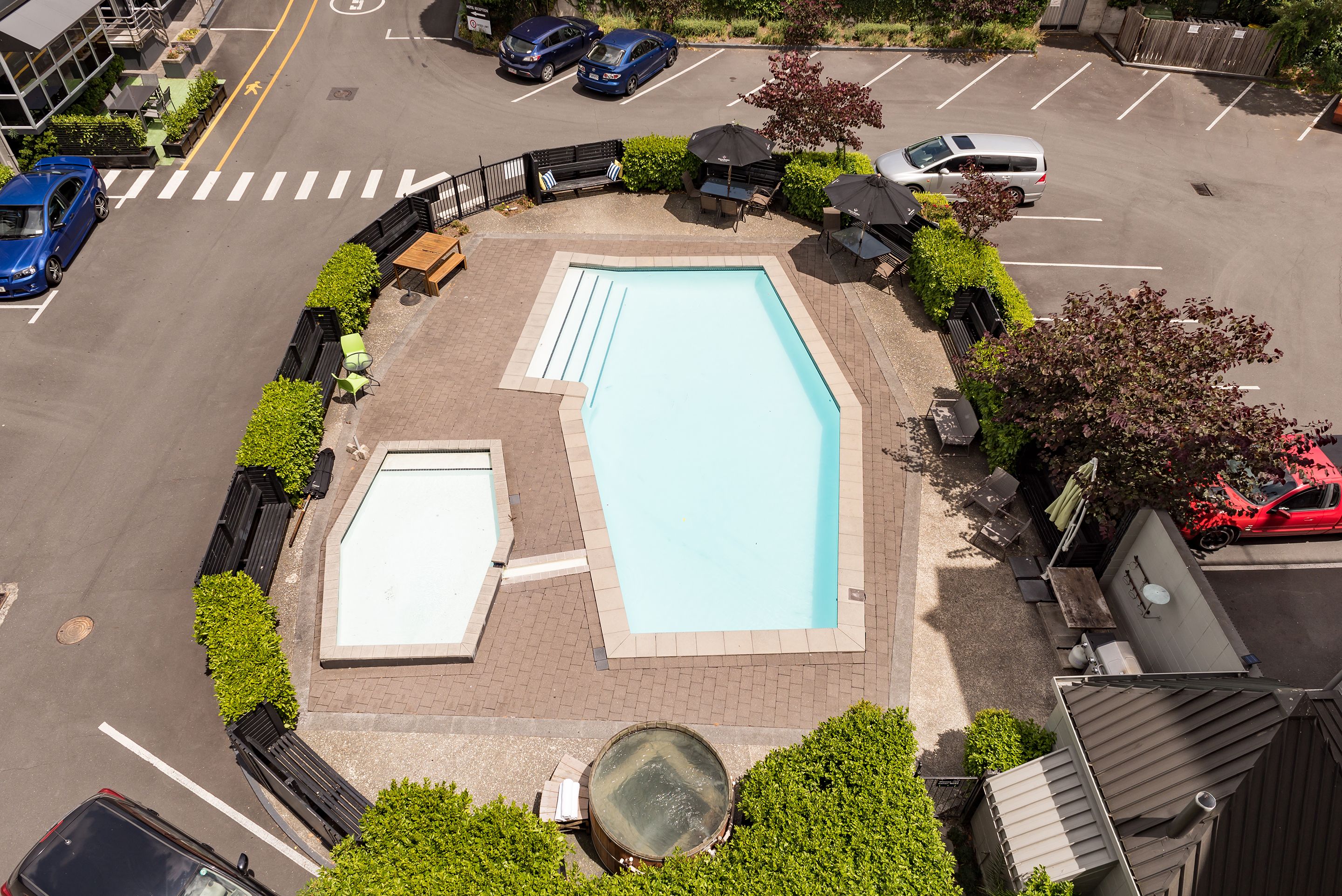 An aerial view of a swimming pool surrounded by a landscaped area with seating and umbrellas.