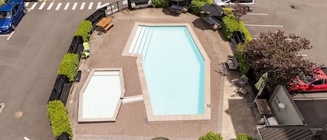 Vista aérea de una piscina rodeada de jardines, mobiliario y sombrillas.