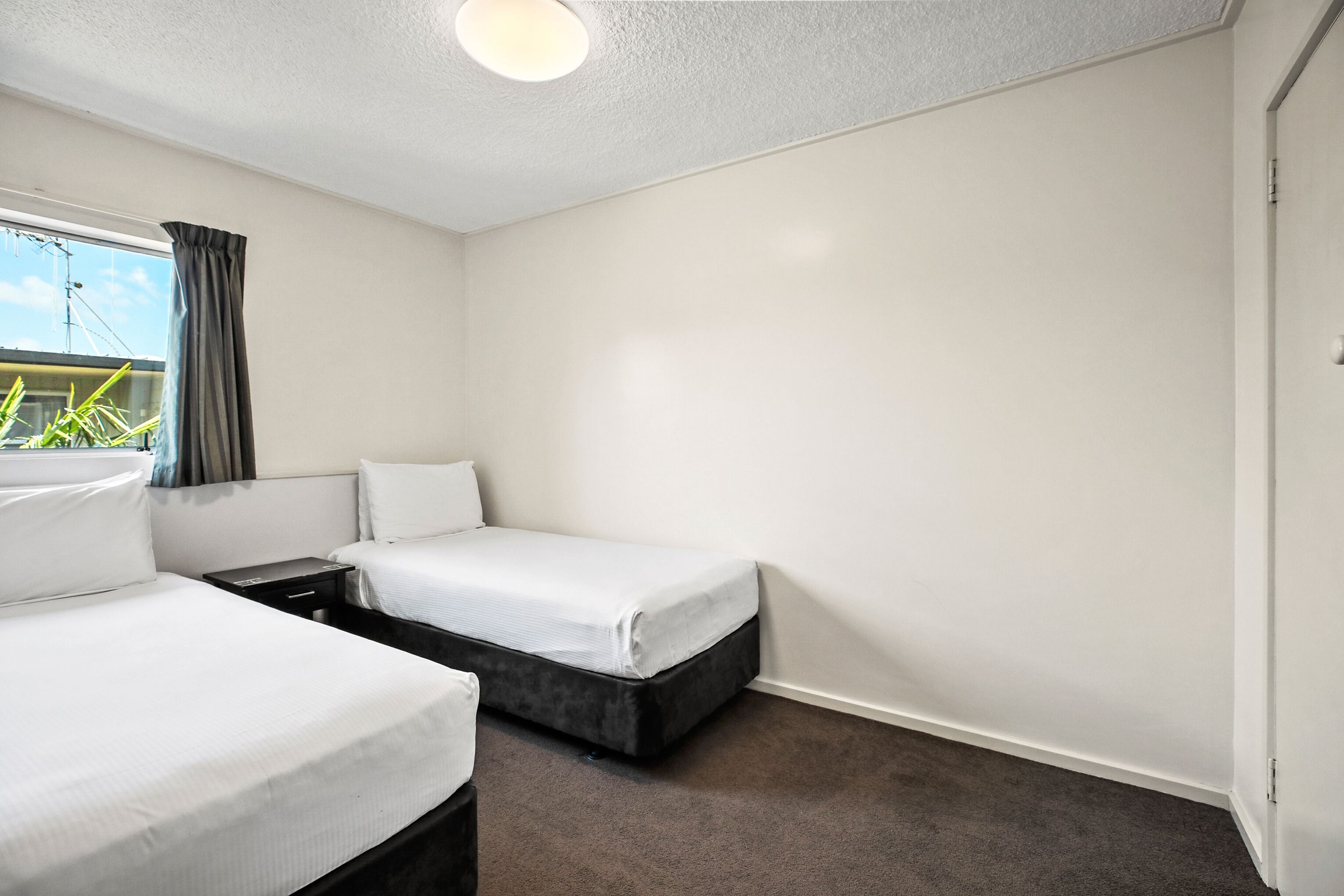 A hotel room with two single beds, a small table, and a window with curtains.