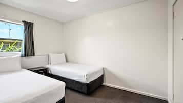 Habitación de hotel con dos camas individuales, una mesita y un ventanal con cortinas.