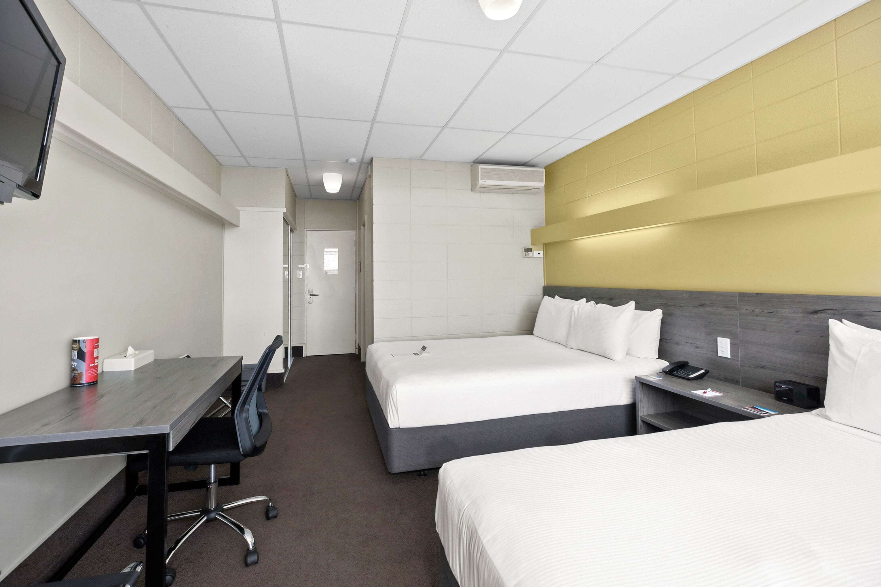 Une chambre d’hôtel avec deux lits, un bureau, une chaise, une télévision et une table de chevet avec un téléphone.