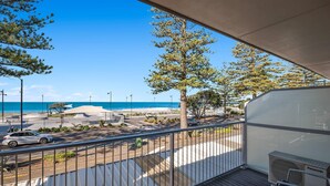 A balcony with a view of the beach, a parked car, and a Panasonic air conditioner.