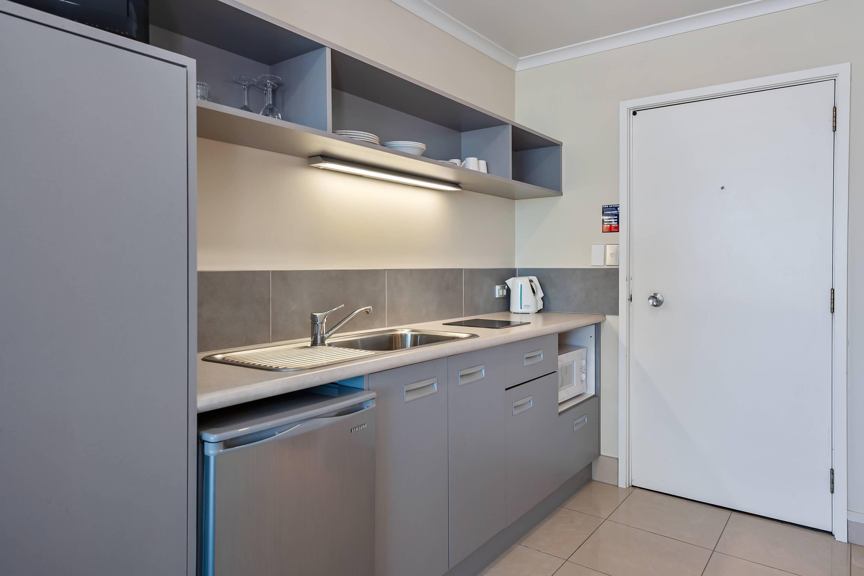 A modern kitchen with grey cabinets, a built-in dishwasher, a sink, and a coffee machine.