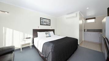 Una habitación de hotel con cama, mesita de noche, silla, kitchenette y ventana.