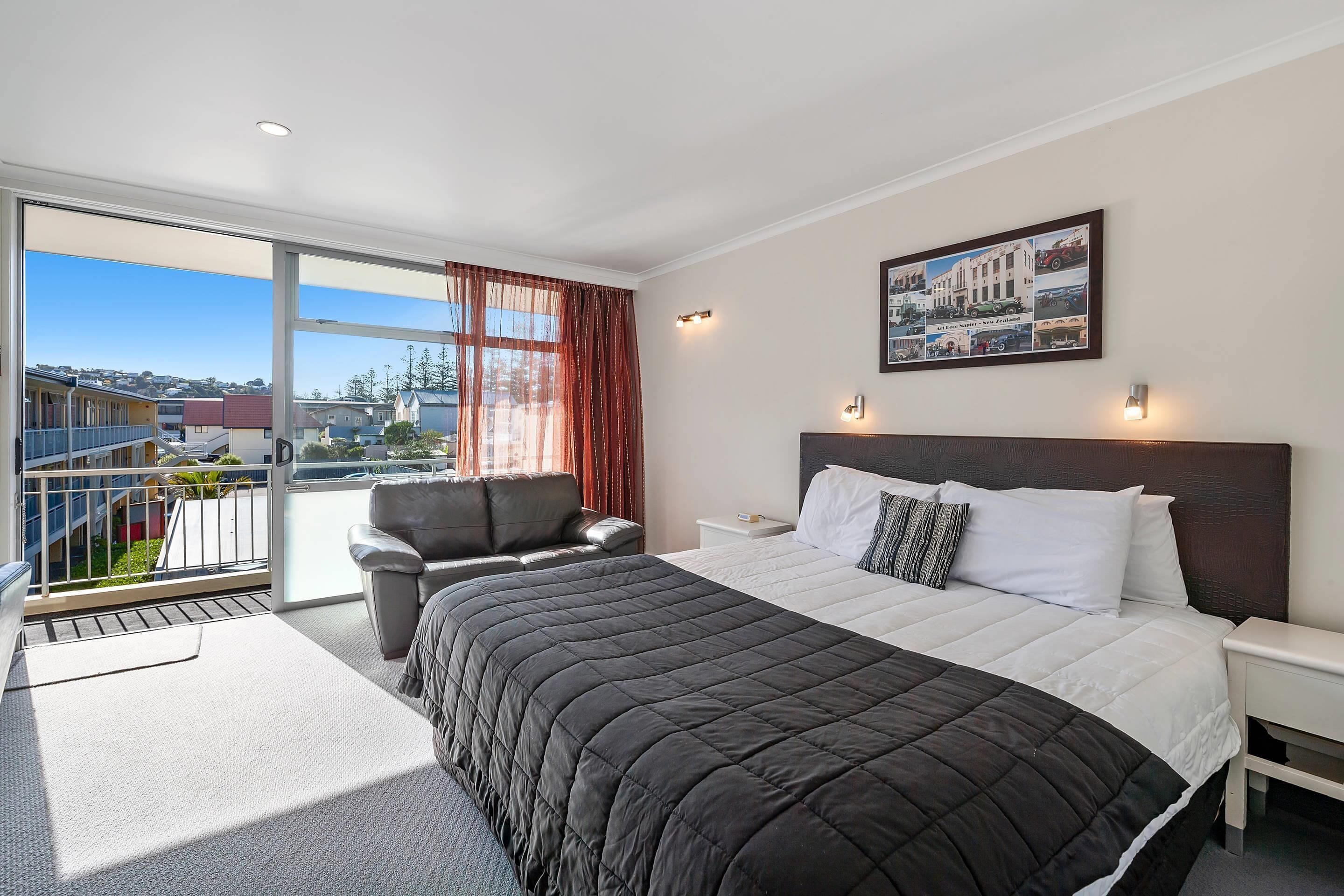 Habitación de hotel con una cama grande, una silla, una mesita de noche y un ventanal con vistas al exterior.