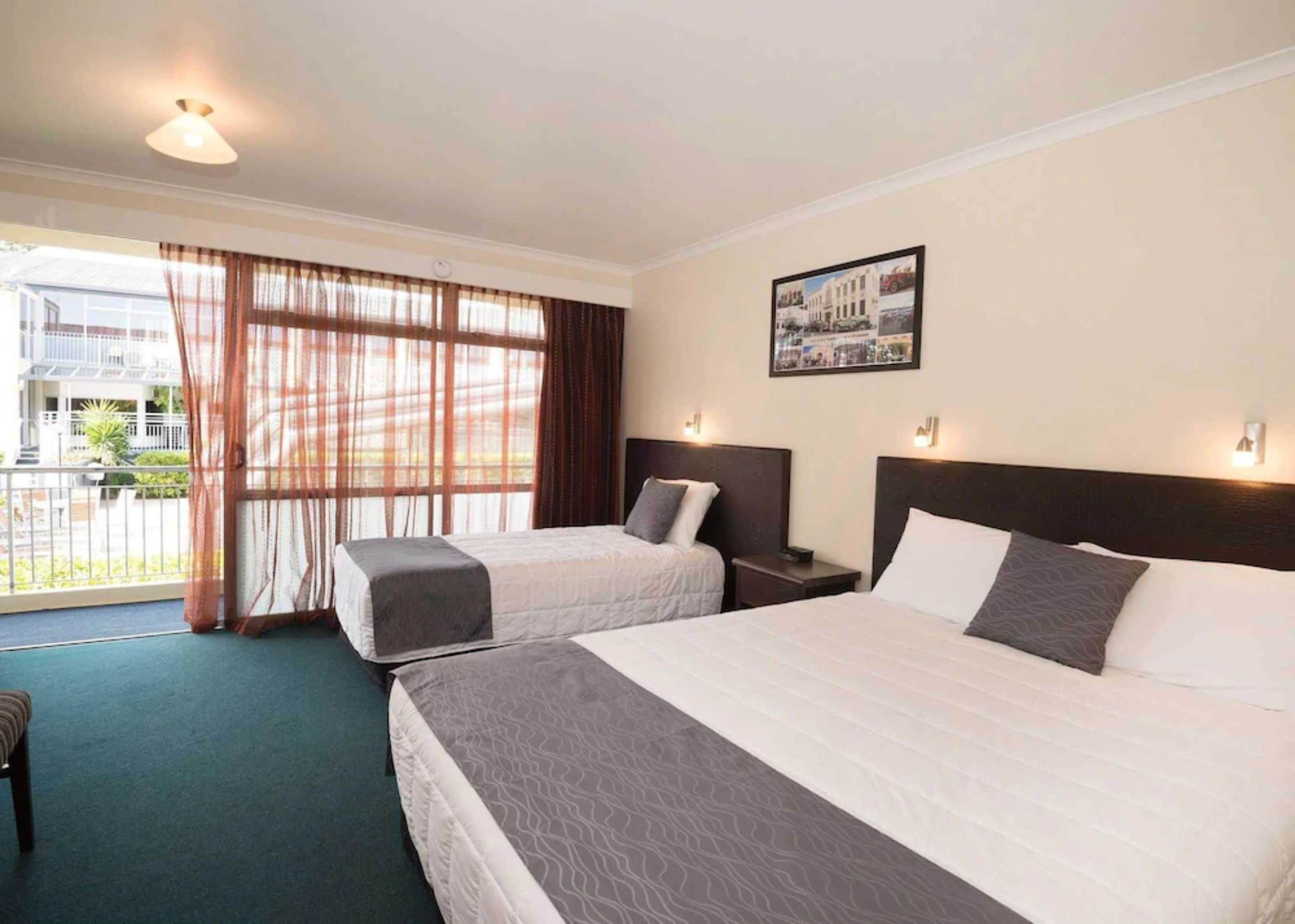 A hotel room with two beds, a balcony, and a cityscape view.