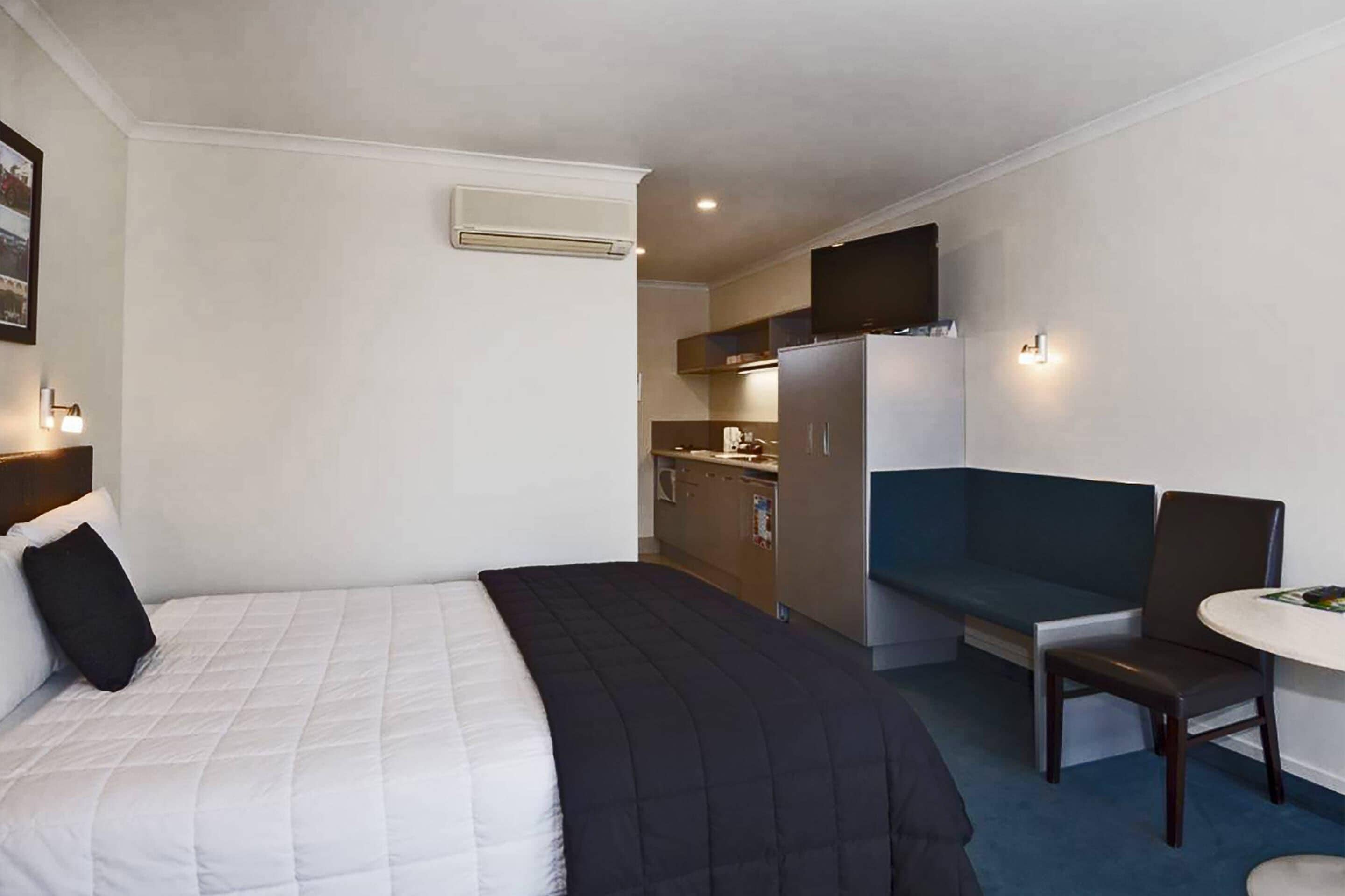 Une chambre d’hôtel comprenant un lit, une petite kitchenette, un coin salon avec une table et des chaises, et un téléviseur fixé au mur.