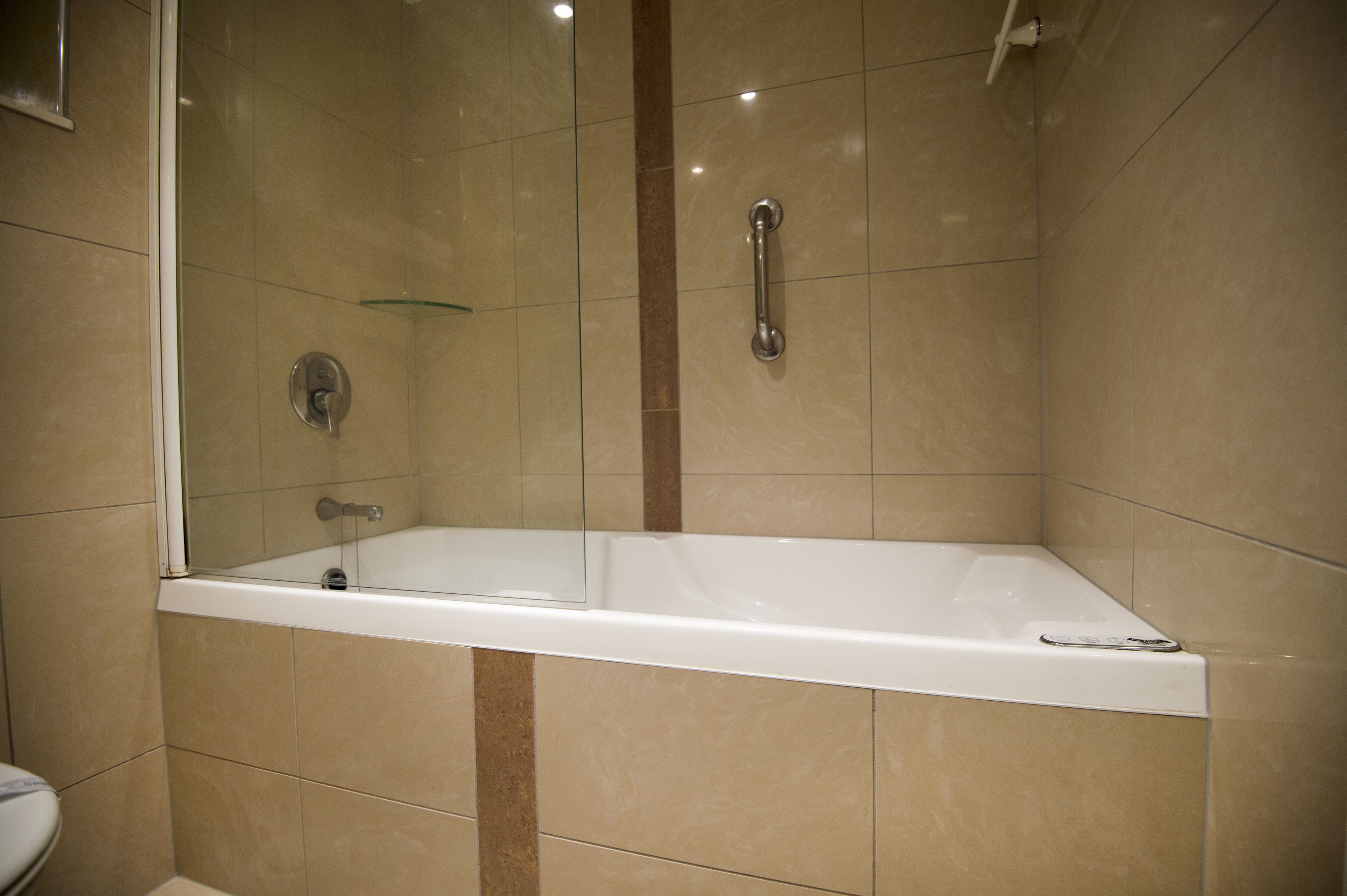A modern bathroom with a glass-enclosed shower, a white bathtub, and beige tiles.