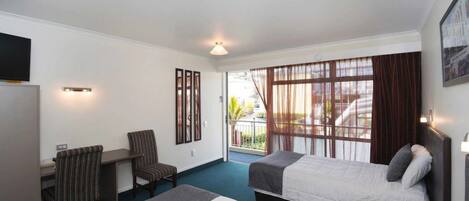 Habitación de hotel con dos camas, un escritorio con silla, televisión y ventana con cortinas.