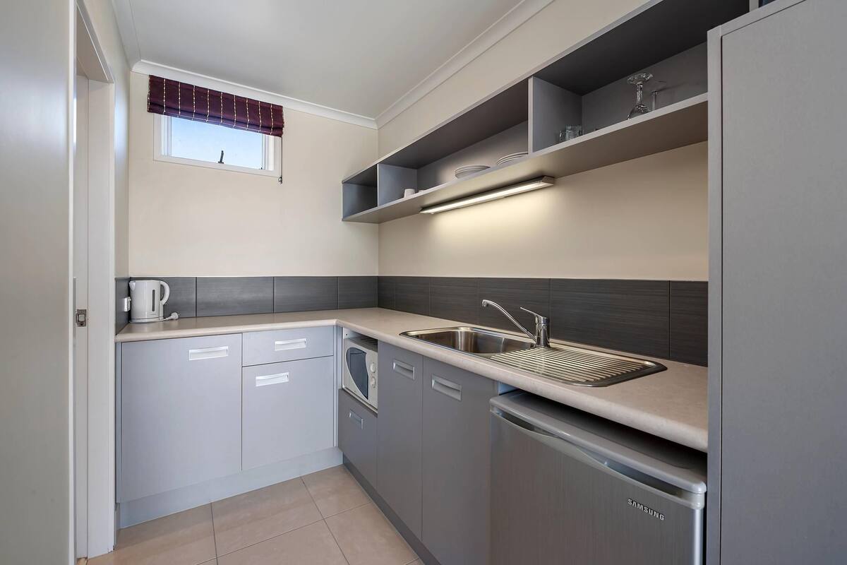 Una cocina moderna con armarios grises, lavavajillas integrado y una ventana con cortinero.