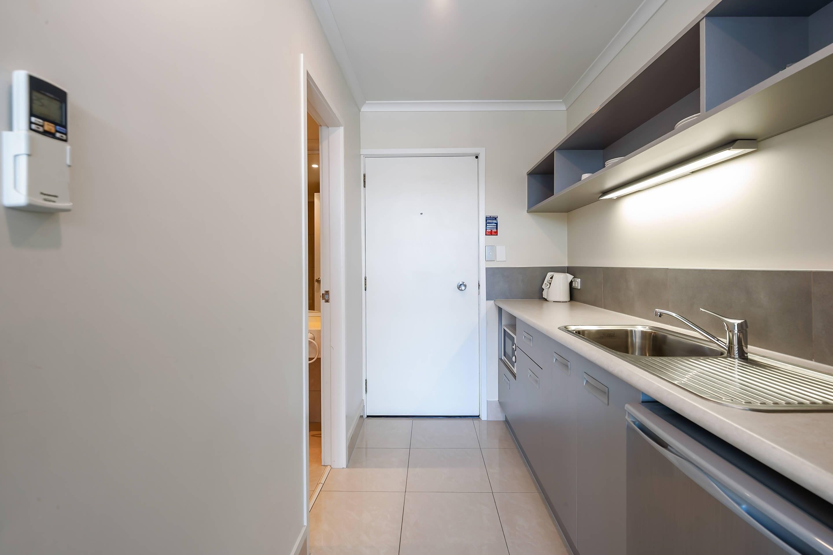 A modern kitchen with a built-in dishwasher, stainless steel sink, and a digital thermostat on the wall.
