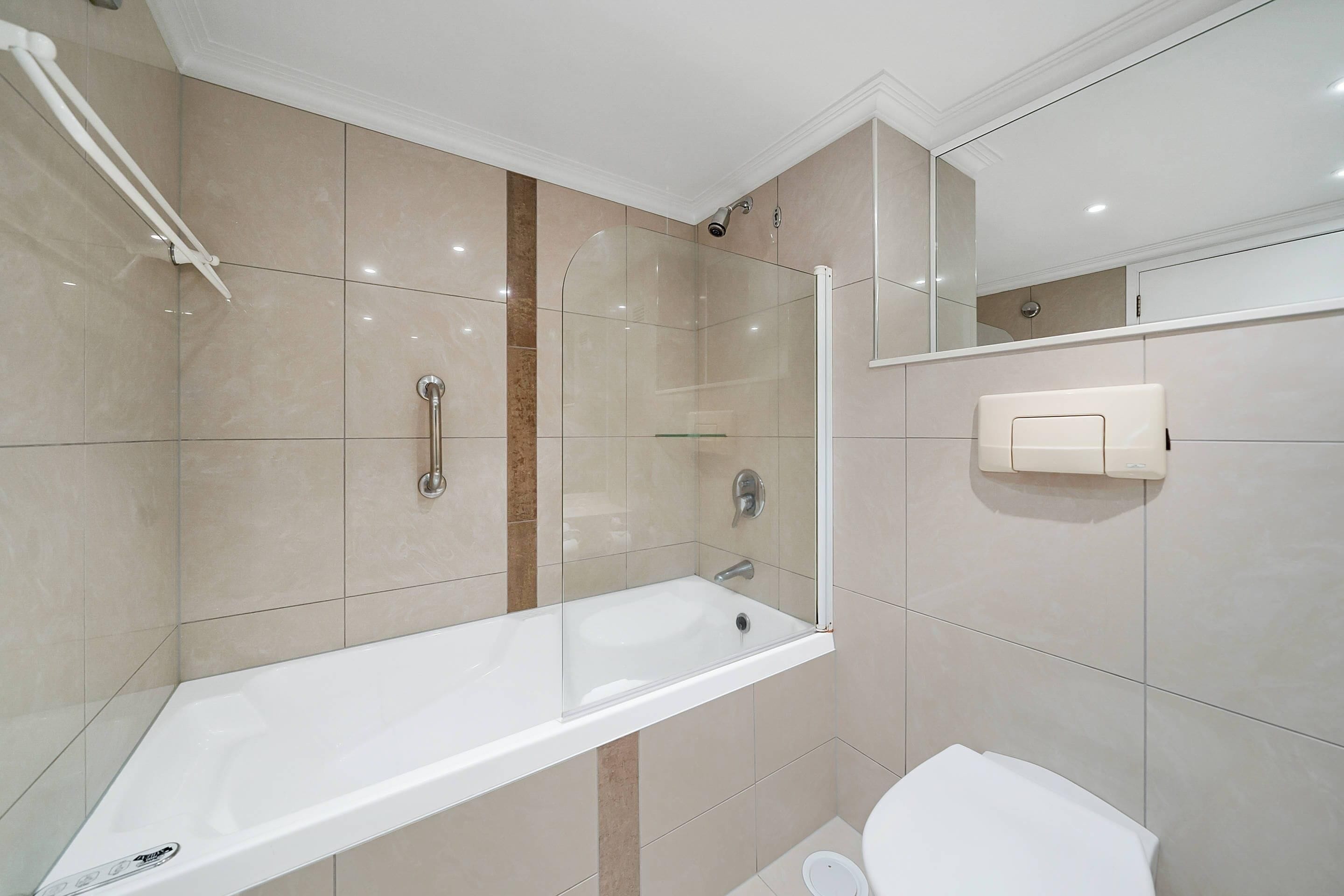 A modern bathroom with a glass-enclosed shower, a white bathtub, and a toilet.