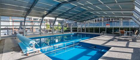 Una piscina interior con techo de cristal, zona de piscina despejada y un puesto de socorrista.