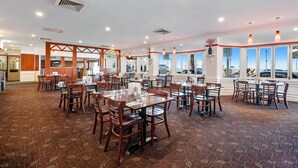 A spacious dining area with multiple tables and chairs, large windows offering views, and a patterned carpet.