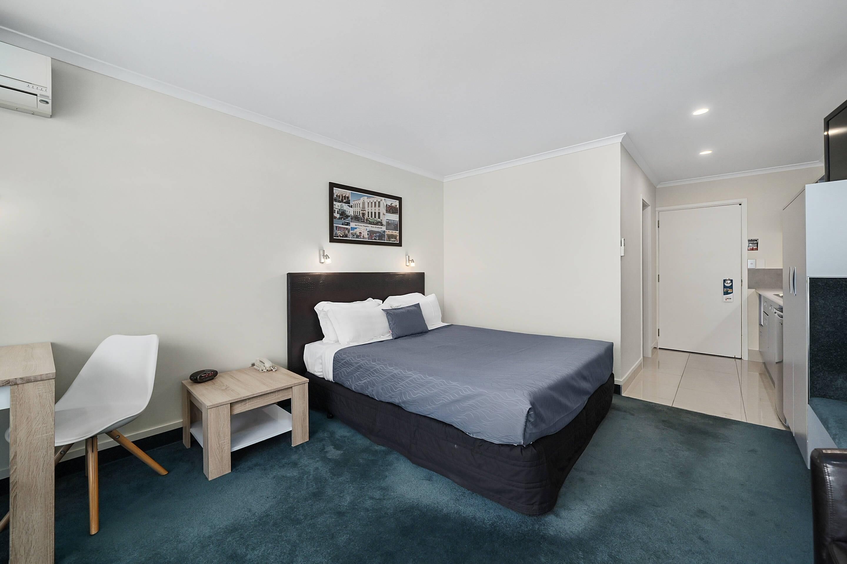 Ein Hotelzimmer mit Bett, Schreibtisch, Stuhl, kleinem Tisch und einem Bild an der Wand.