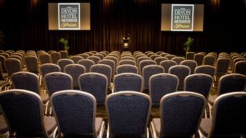 Ein Konferenzraum mit Reihen von Stühlen und zwei Bildschirmen, die die Marke 'The Devon Hotel New Plymouth Heritage' zeigen.
