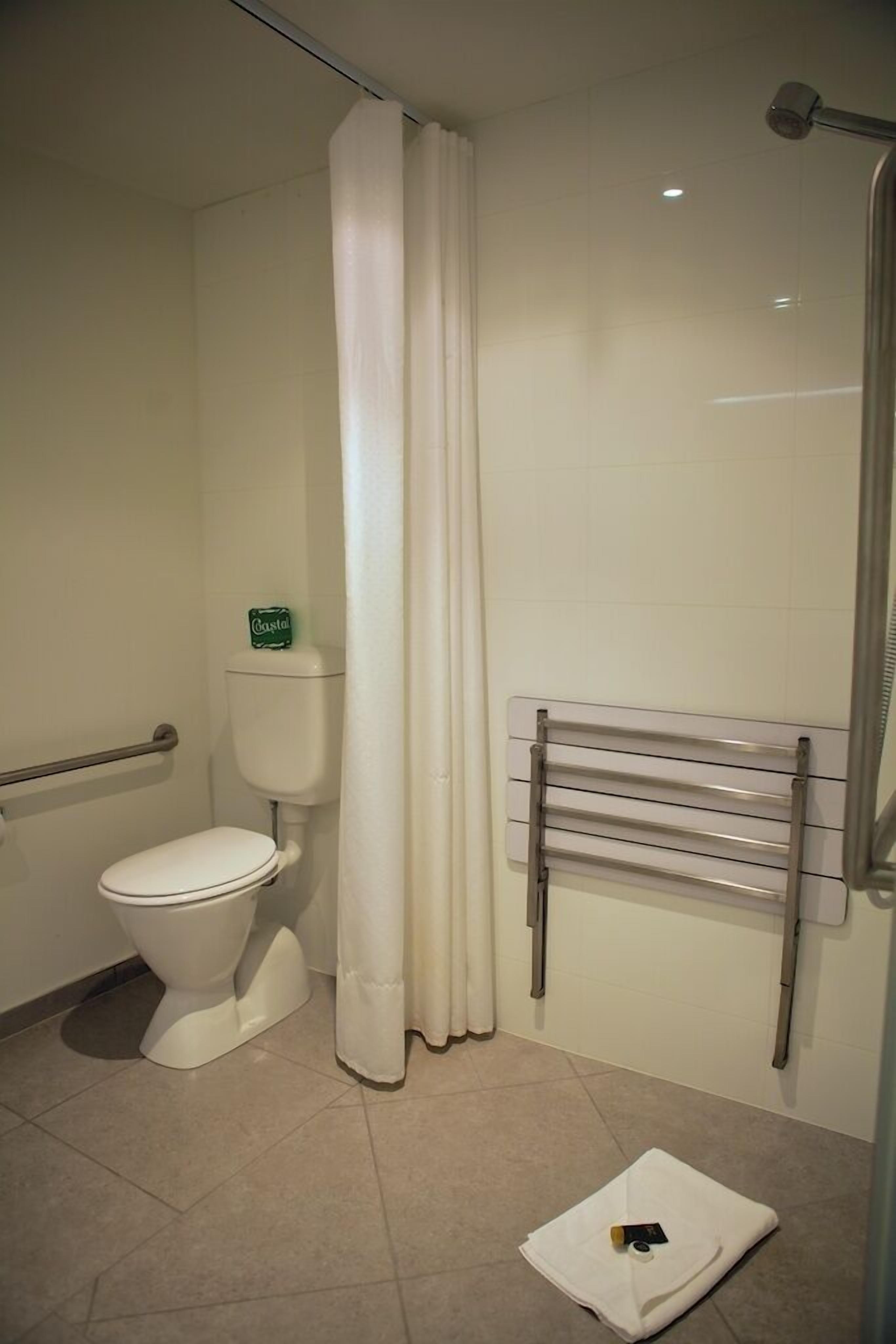 Une salle de bain équipée d’un WC, d’un rideau de douche, d’un porte-serviettes et d’un support à papier toilette.