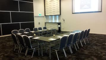 Una sala conferenze con un lungo tavolo, sedie, uno schermo per proiettore e una parete con motivo decorativo.
