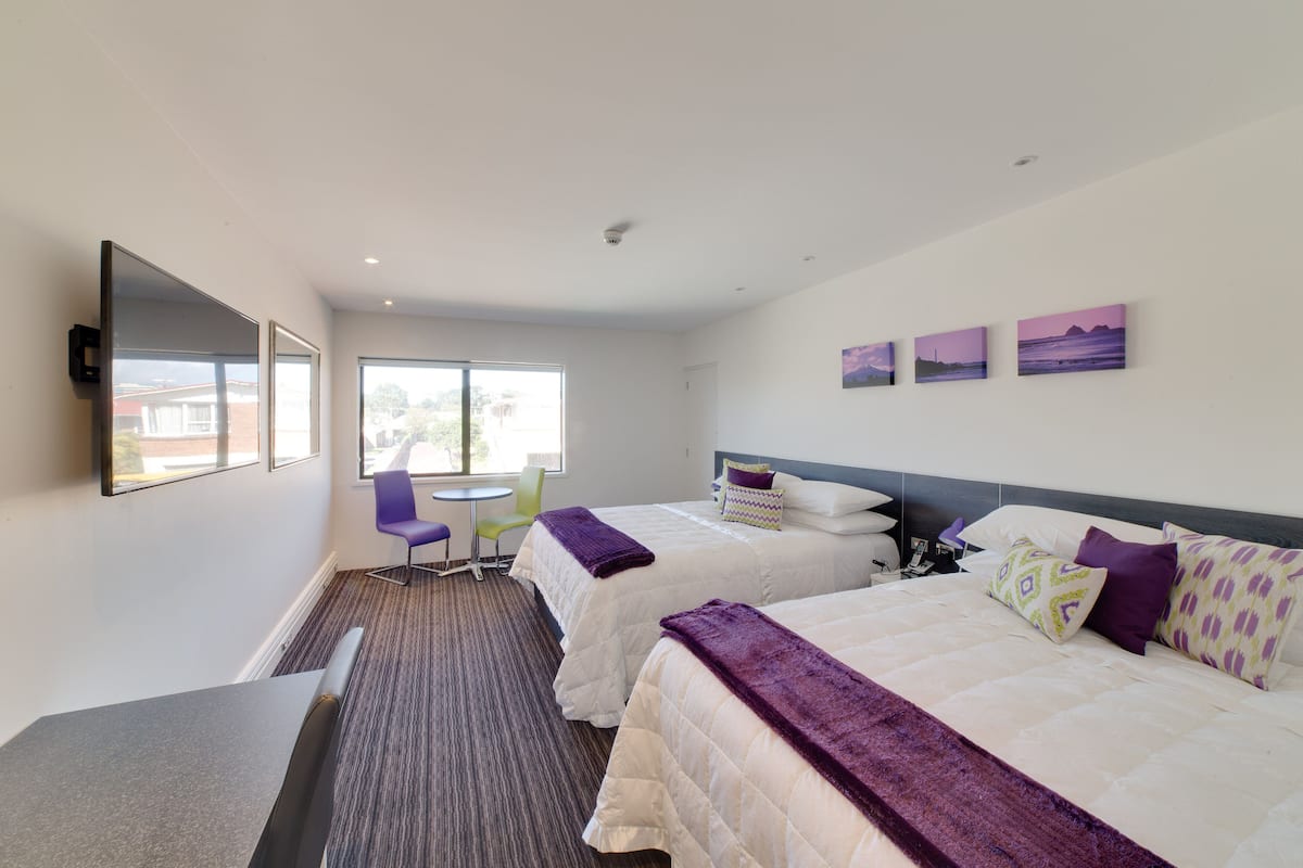 Habitación de hotel con dos camas, un escritorio, una silla y una ventana.