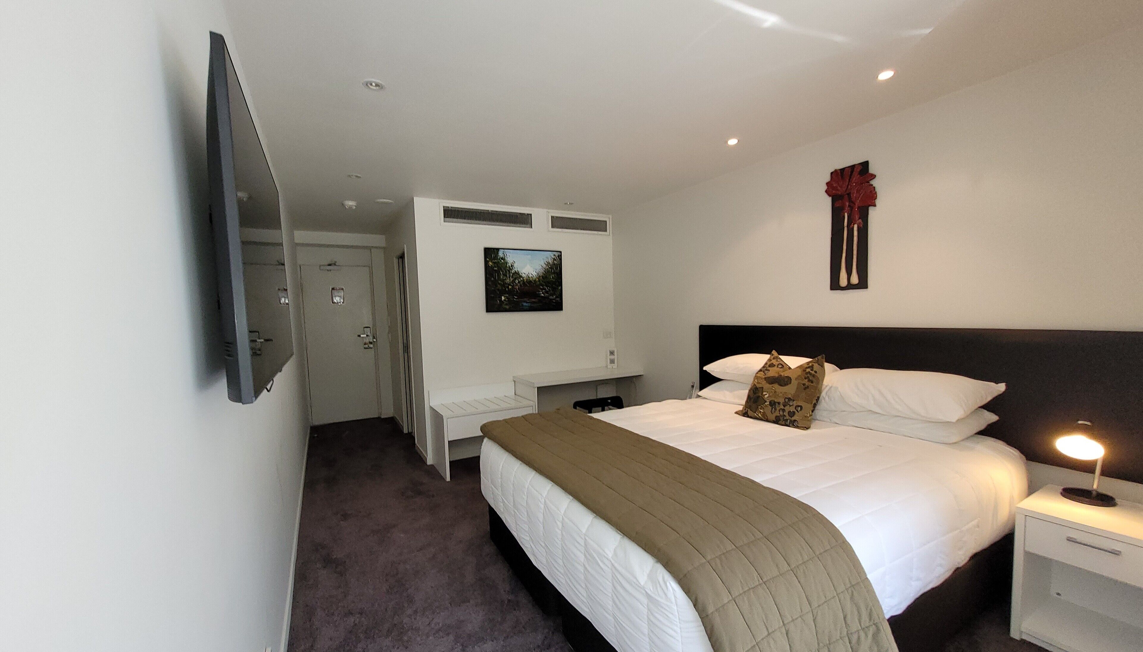 A hotel room with a bed, bedside table, lamp, and a painting on the wall.