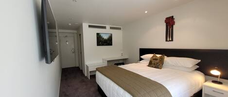A hotel room with a bed, bedside table, lamp, and a painting on the wall.