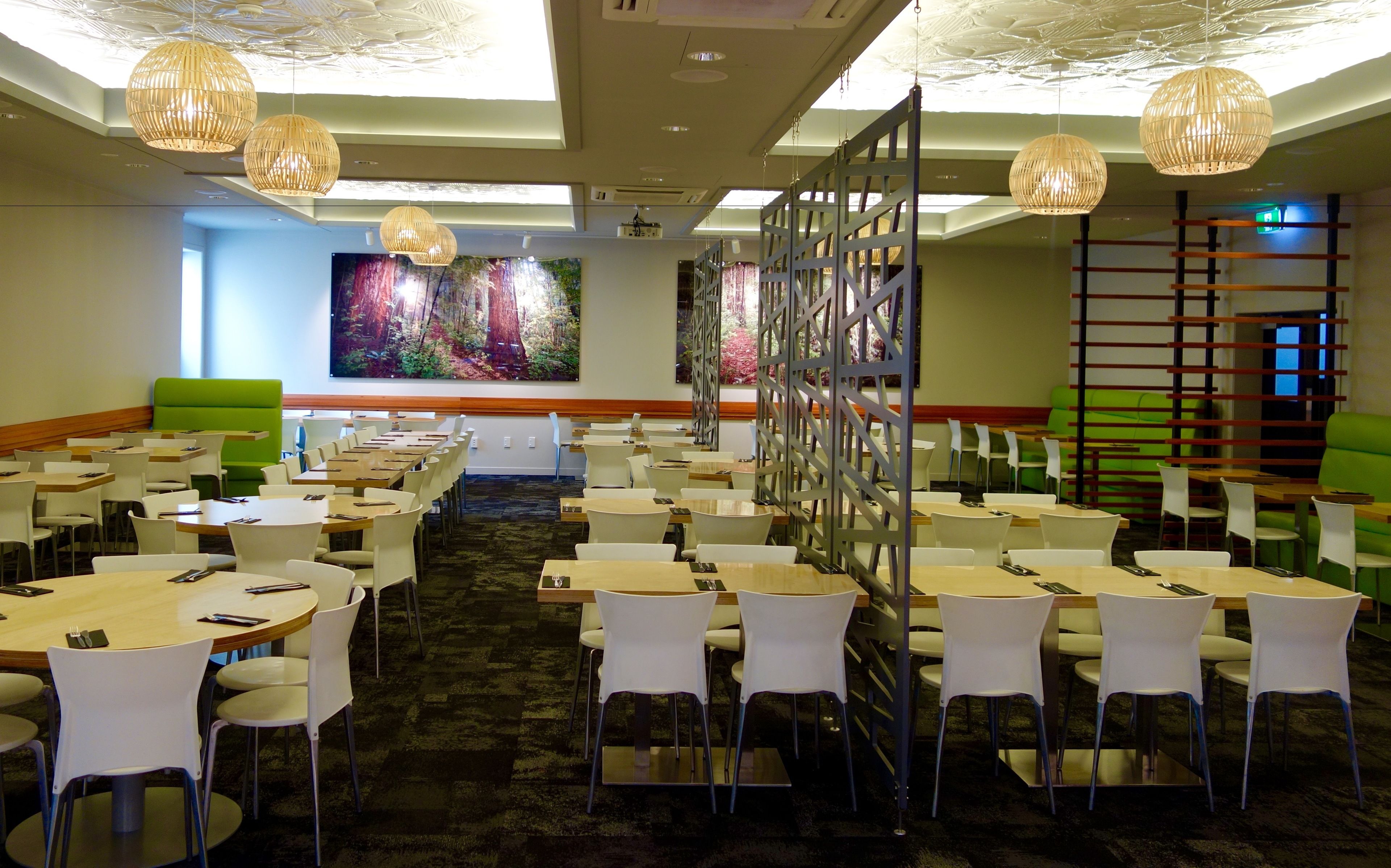 A conference room with multiple tables and chairs, a large screen, and decorative lighting.