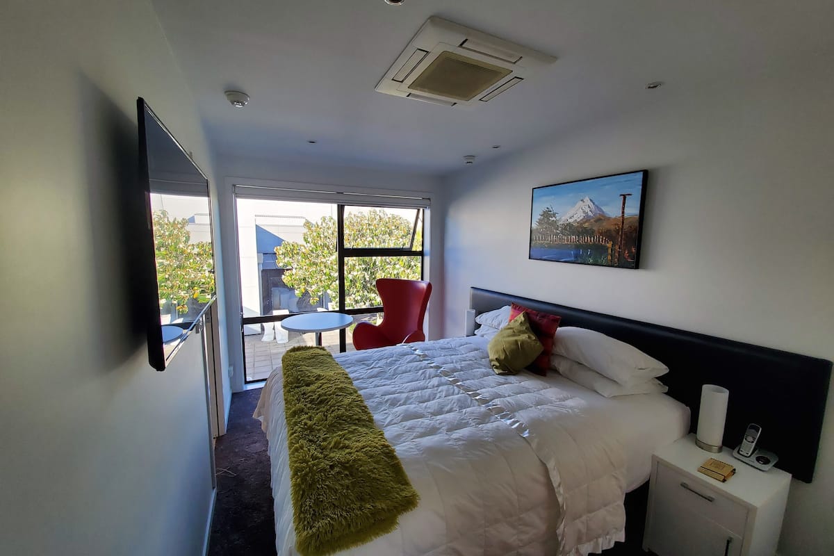 Una habitación de hotel con una cama, una mesita de noche, una silla, una ventana y un cuadro en la pared.