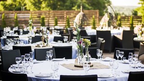 Un área de comedor al aire libre con mesas redondas dispuestas para una comida, rodeada de sillas.