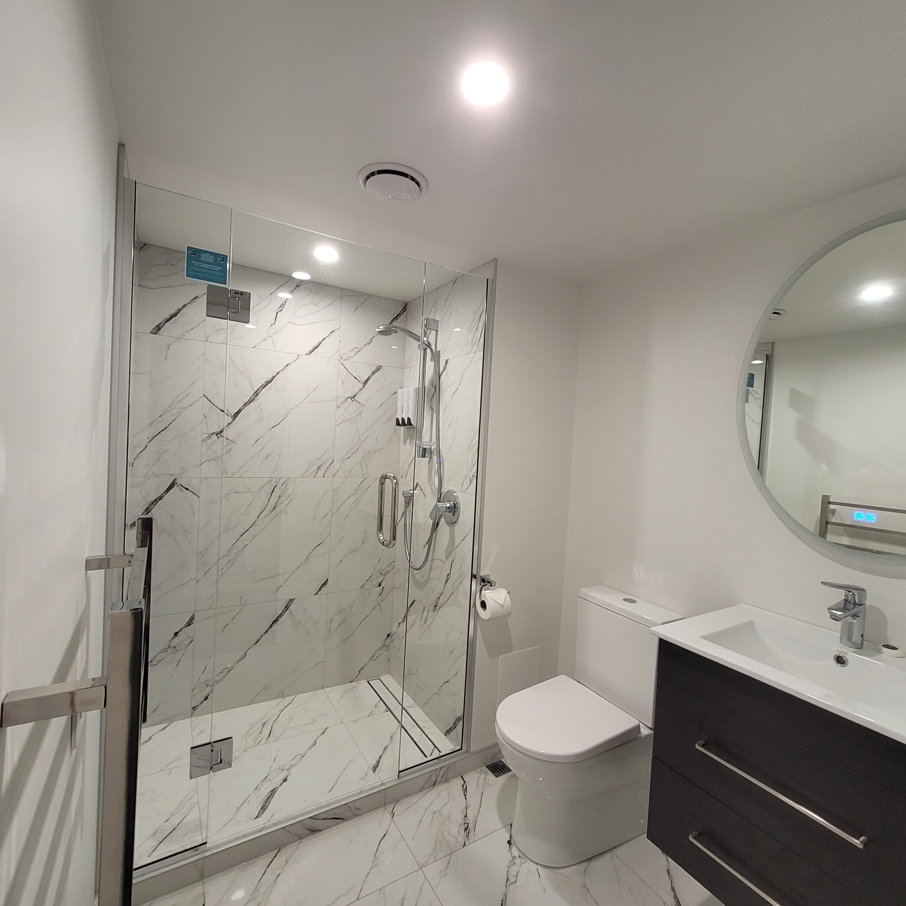 Ein modernes Badezimmer mit einer gläsernen Dusche, einer weißen Toilette, einem Waschtisch mit Spiegel und Marmorböden.