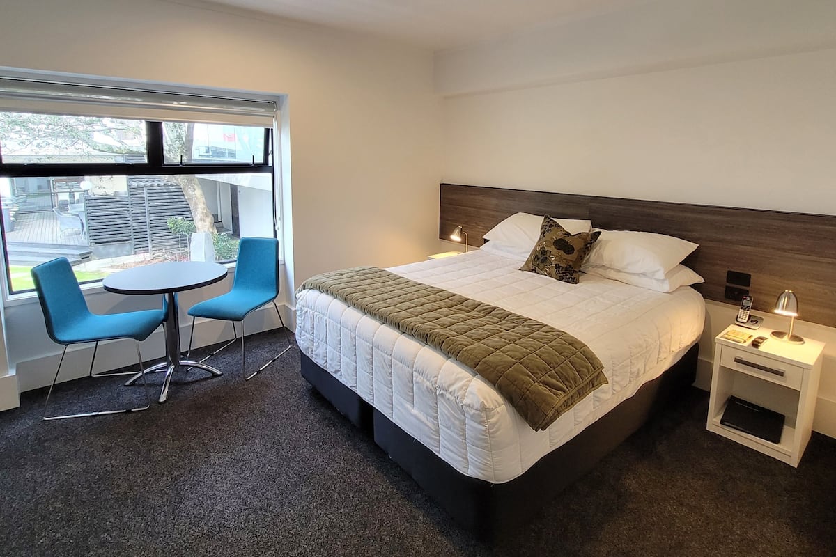 Una habitación de hotel con cama, mesita de noche, lámpara y una pequeña mesa con dos sillas.