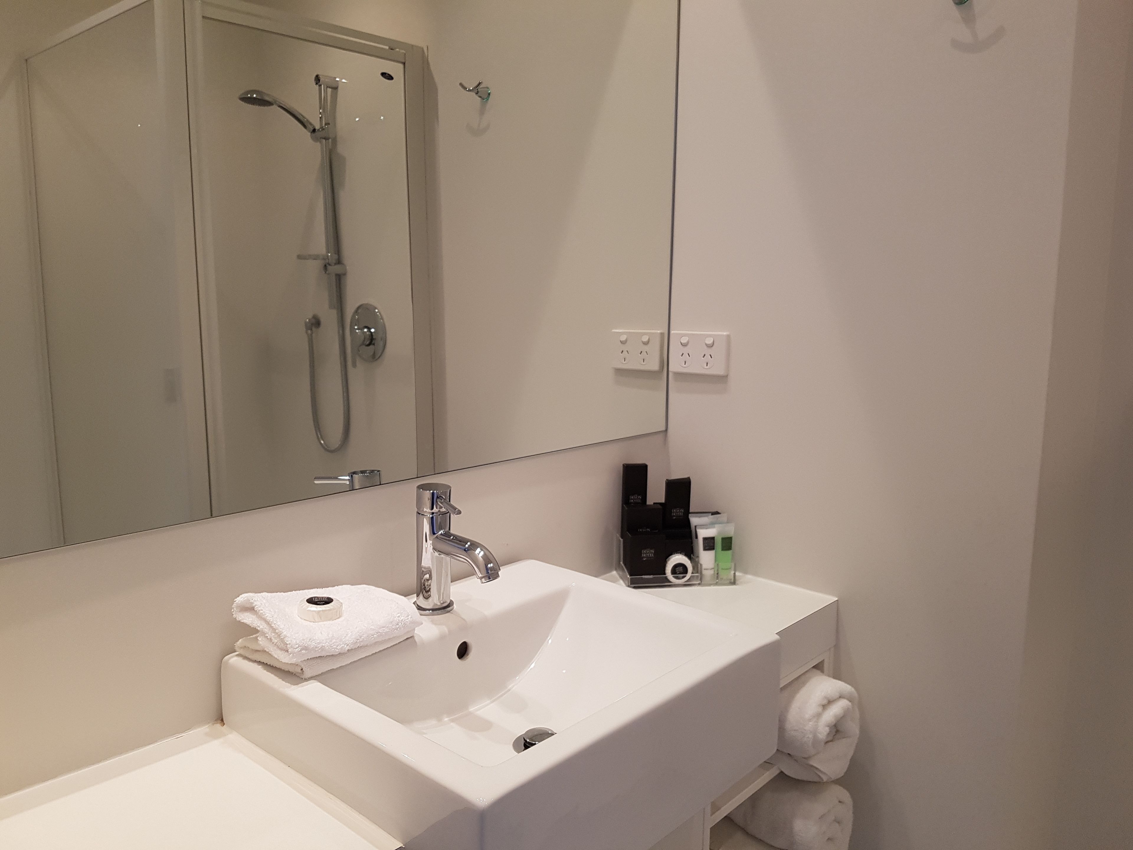 A bathroom with a white sink, a mirror, a shower, and a towel rack.