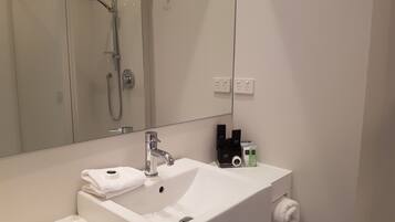 A bathroom with a white sink, a mirror, a shower, and a towel rack.