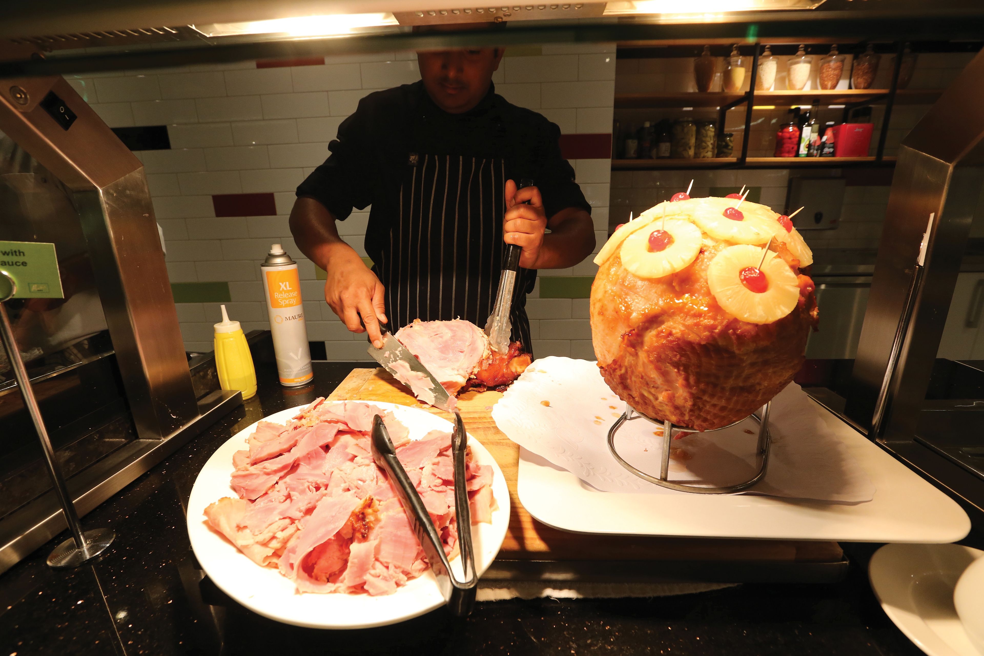 A chef preparing food in a kitchen with a large meat centerpiece, a cutting board, and various kitchen utensils.