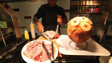 A chef preparing food in a kitchen with a large meat centerpiece, a cutting board, and various kitchen utensils.