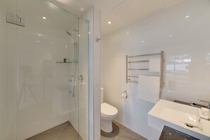 Un baño moderno con cabina de ducha de vidrio, inodoro blanco y lavamanos empotrado con tocador.