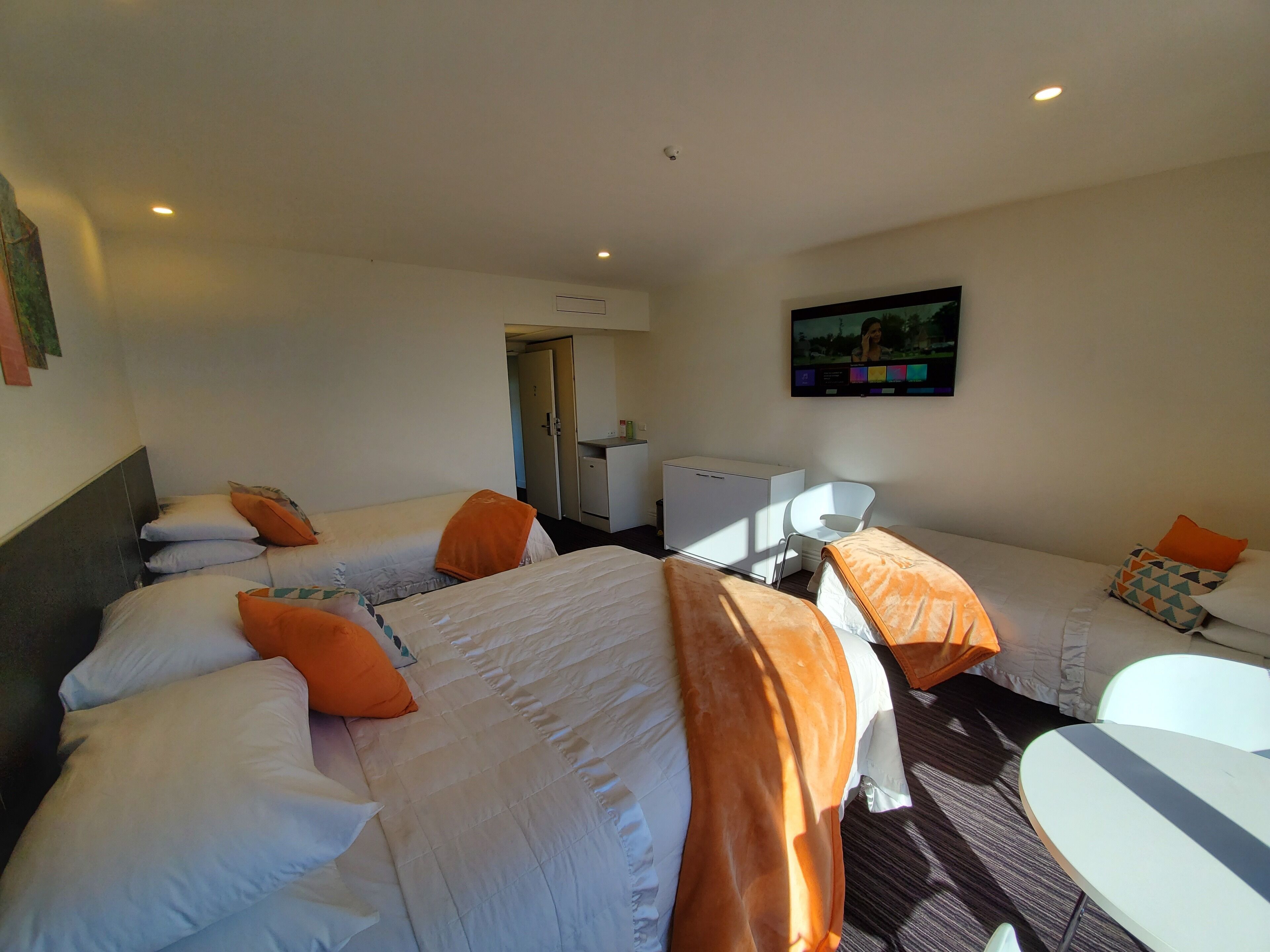 Ein Hotelzimmer mit zwei Betten, einer kleinen Küchenzeile, einem Fernseher und einem Esstisch.