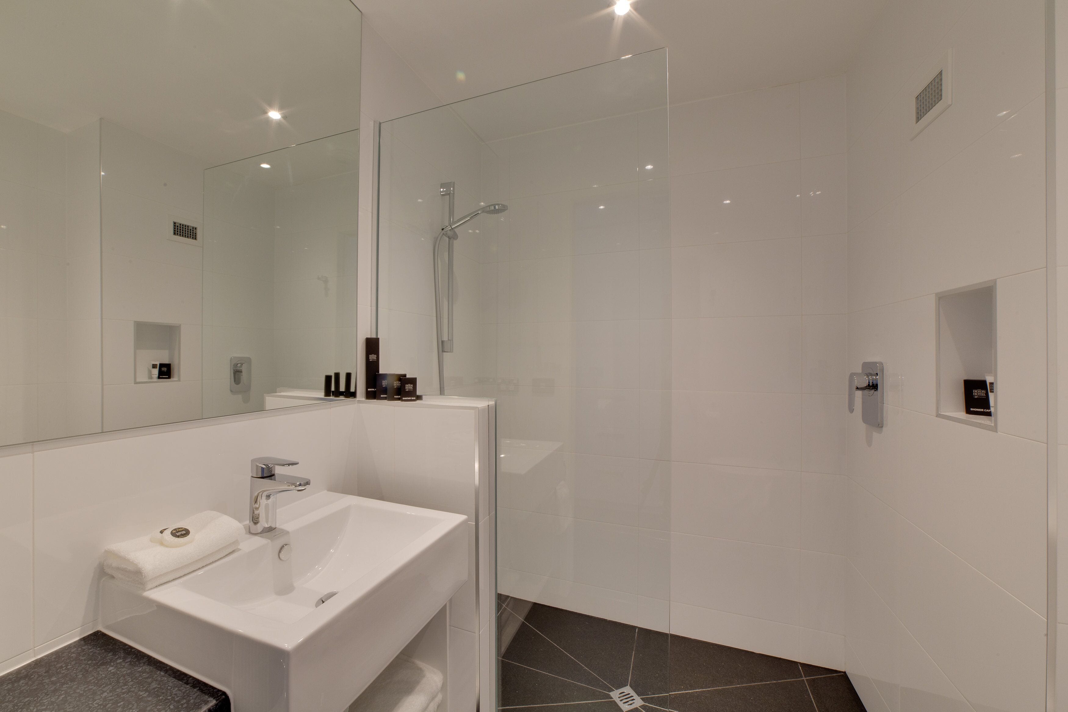 Un baño moderno con un lavamanos blanco, una cabina de ducha de vidrio y un espejo grande.