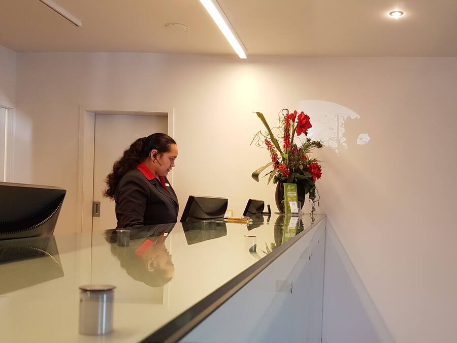 A reception desk with a laptop, a vase of flowers, and a door in the background.